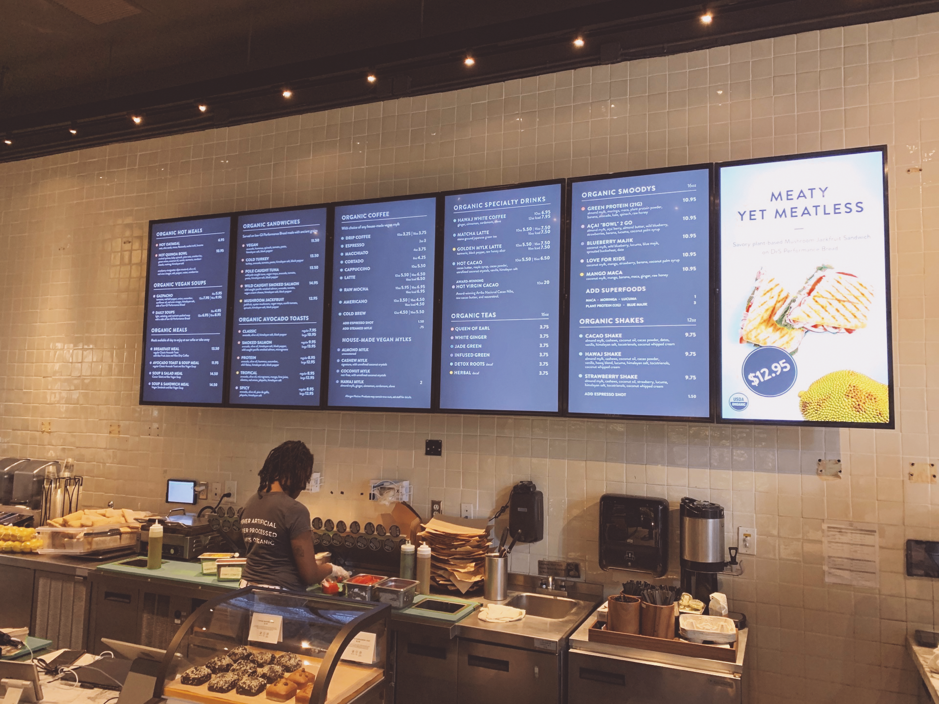 Six digital menu boards above a food prep counter